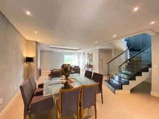 Ambiente interno com mesa de vidro e escadaria em uma residência.
