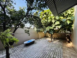 Vista de um pátio externo com piso de tijolos e vegetação exuberante.