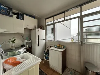 Vista interna de uma cozinha com armários brancos e janela grande.