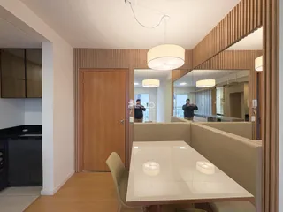 Interior de uma sala de jantar com piso de madeira clara e espelho refletindo o ambiente.