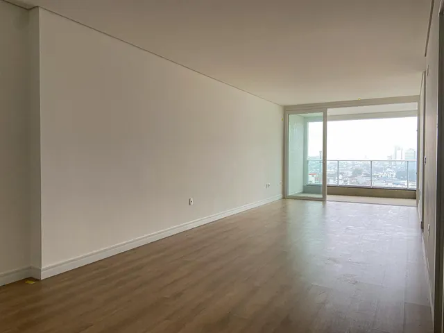 Ambiente interno de uma sala ampla com piso de madeira e vista panorâmica da cidade.