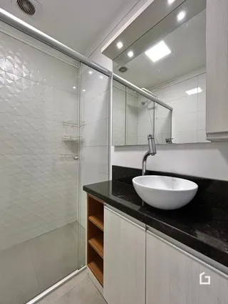 Interior de um banheiro moderno com box de vidro e bancada escura.