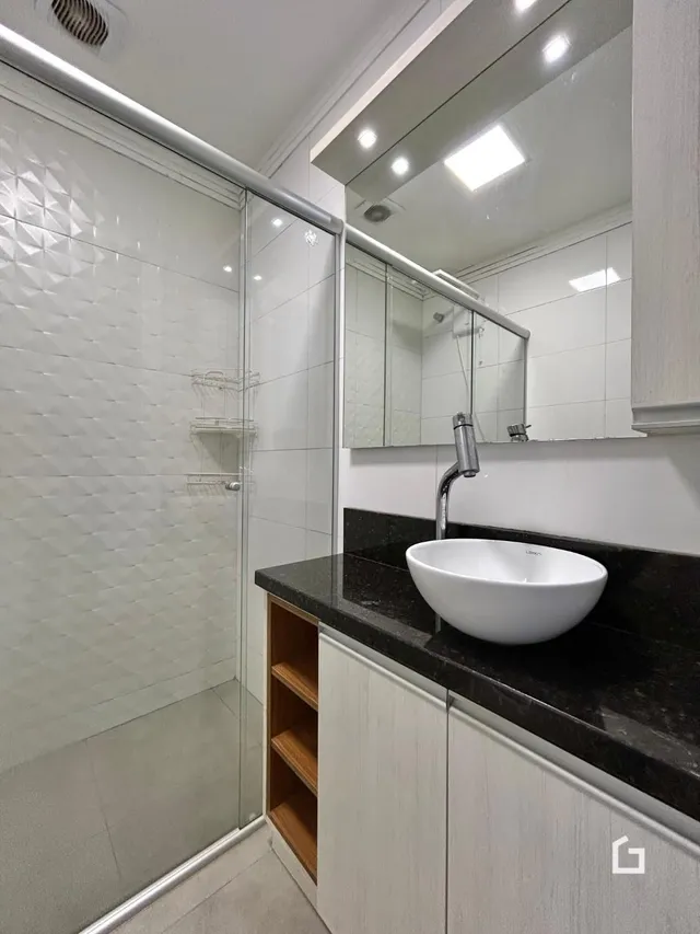 Interior de um banheiro moderno com box de vidro e bancada escura.