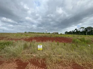 Vista de uma paisagem de campo seco com vegetação rasteira e uma estrutura no horizonte.