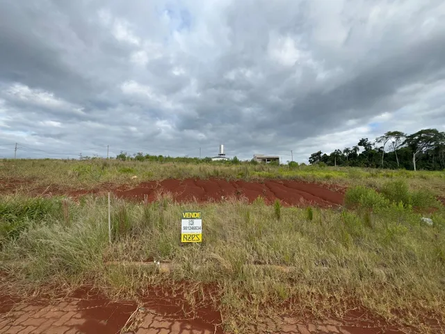 Vista de uma paisagem de campo seco com vegetação rasteira e uma estrutura no horizonte.