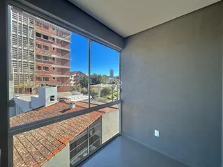 Vista da janela de um imóvel em Lajeado, Brasil, mostrando telhados e edifícios ao fundo.
