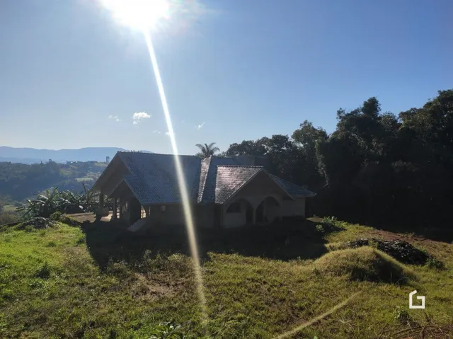 A fachada da casa está situada em uma área verde com vegetação ao redor.