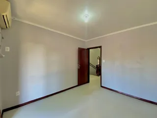 Um corredor interno com paredes brancas e piso de madeira.