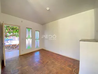 Uma sala de estar com piso de madeira e duas janelas iluminadas.