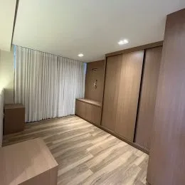 Ambiente interno com piso de madeira e cortinas brancas em um imóvel.