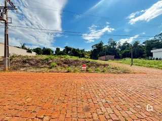 Vista externa de um terreno com piso de tijolos avermelhados e vegetação.