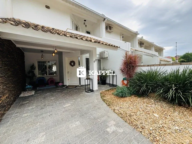 Fachada de uma casa branca em Lajeado, Brasil, com área externa pavimentada e jardim.
