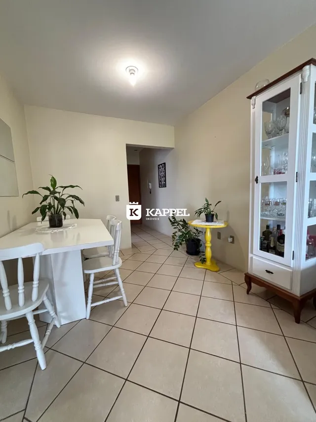 Uma sala de jantar clara com mesa branca e cadeiras brancas, decorada com plantas.