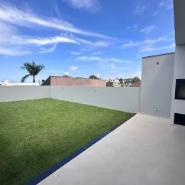 Foto de uma área externa com gramado verde e muro branco.