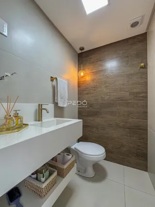 Banheiro moderno com bancada branca e revestimento de parede em tons terrosos.