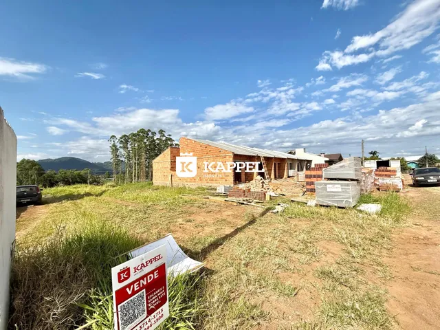 Vista externa de uma construção em terreno aberto com vegetação ao fundo.