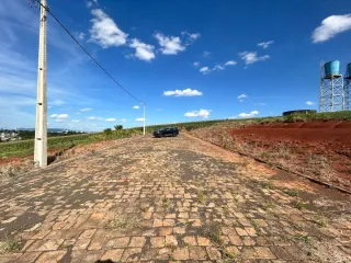 Vista externa de uma área pavimentada com terra vermelha sob um céu azul.