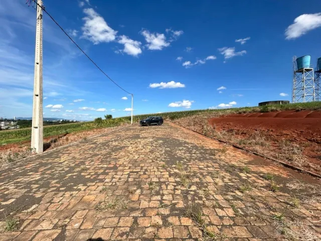 Vista externa de uma área pavimentada com terra vermelha sob um céu azul.