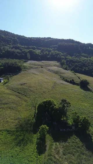 Vista aérea de uma propriedade com colinas verdes e vegetação.