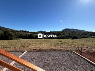 Vista panorâmica de um campo aberto com colinas verdes ao fundo sob um céu azul claro.