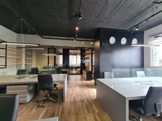 O ambiente apresenta um espaço de escritório com piso de madeira clara.