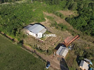Uma vista aérea mostra uma propriedade rural com um grande galpão cercado por vegetação.