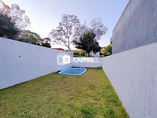 Vista externa mostrando um gramado e uma piscina em um terreno cercado por muros brancos.