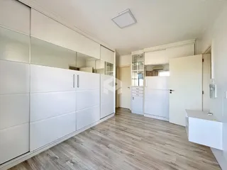 Interior de um ambiente com armários brancos e piso de madeira clara.