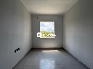 Corredor longo com paredes brancas e uma grande janela mostrando o céu.