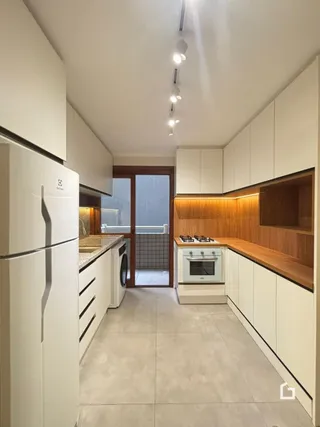 Vista interna de uma cozinha moderna com armários brancos e detalhes em madeira.