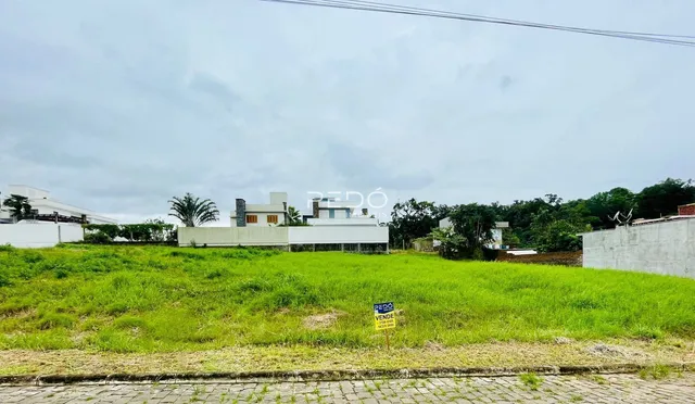 Vista externa de uma propriedade com gramado verde e edificações ao fundo.