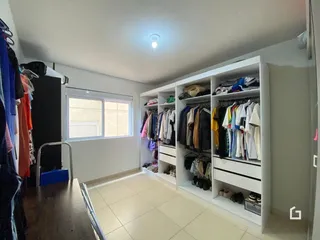 Interior de um cômodo com estantes de roupas brancas e piso de cerâmica.