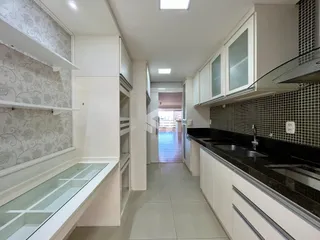 A cozinha apresenta armários brancos e bancadas escuras com revestimento de azulejos.