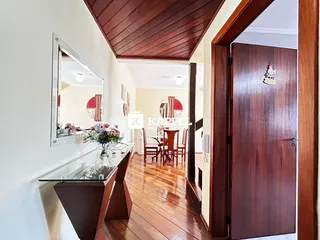 Vista de uma sala com piso de madeira e teto inclinado, mostrando um ambiente bem iluminado.
