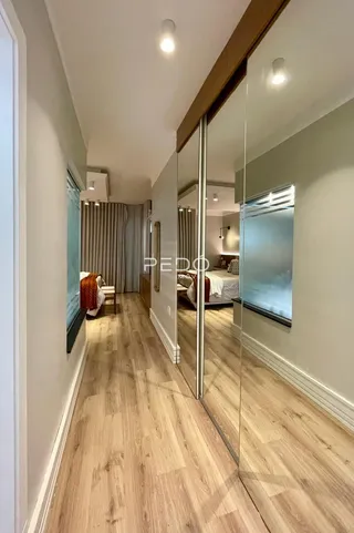 Hall de entrada com piso de madeira clara e espelho refletindo o interior da casa.