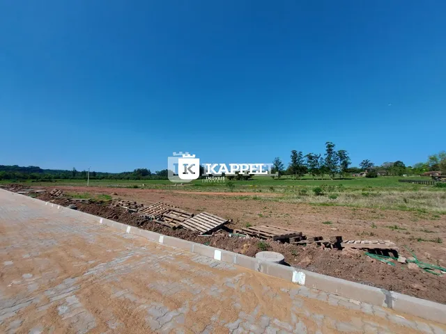 Vista externa de um terreno aberto com campo seco e vegetação ao fundo.