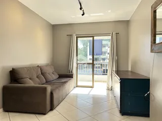 Sala de estar com sofá e porta de vidro abrindo para a varanda.