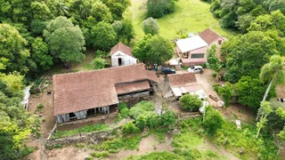 Foto aérea de uma propriedade rural com construções de telhado de telha cercadas por vegetação densa.