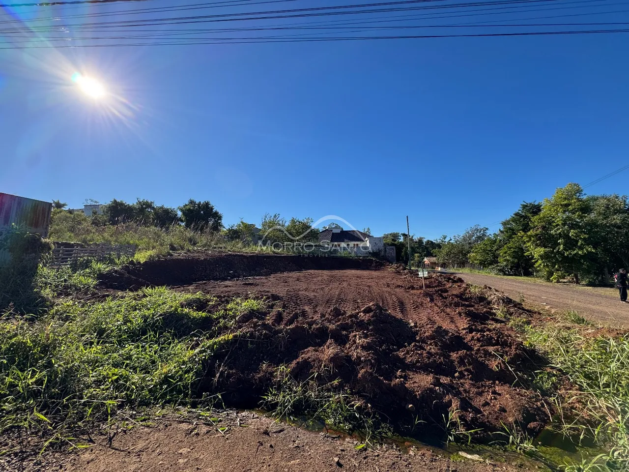 Foto de um terreno aberto com terra escura e vegetação rasteira sob um céu azul.