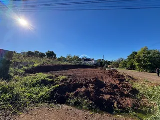 Foto de um terreno aberto com terra escura e vegetação rasteira sob um céu azul.
