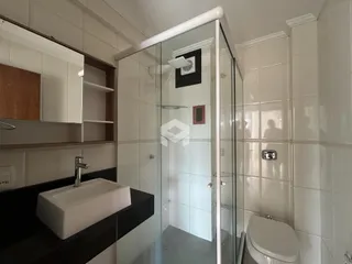 Foto de um banheiro com box de vidro e revestimento cerâmico branco.