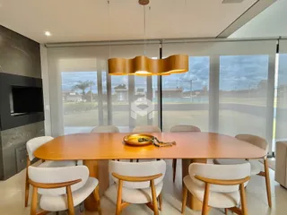 Sala de jantar com mesa de madeira e grandes janelas.