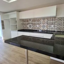 Vista de uma cozinha com armários brancos e bancada escura.