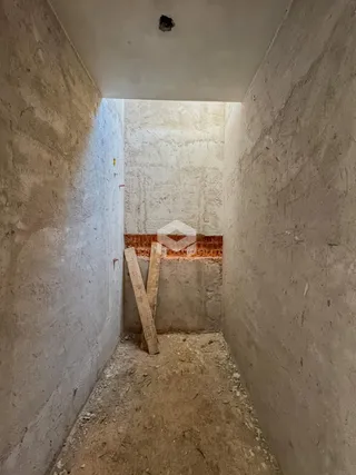 Corredor interno com paredes de alvenaria cruas e vigas de madeira visíveis.