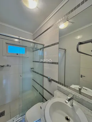 Banheiro com box de vidro e revestimento de azulejos brancos.