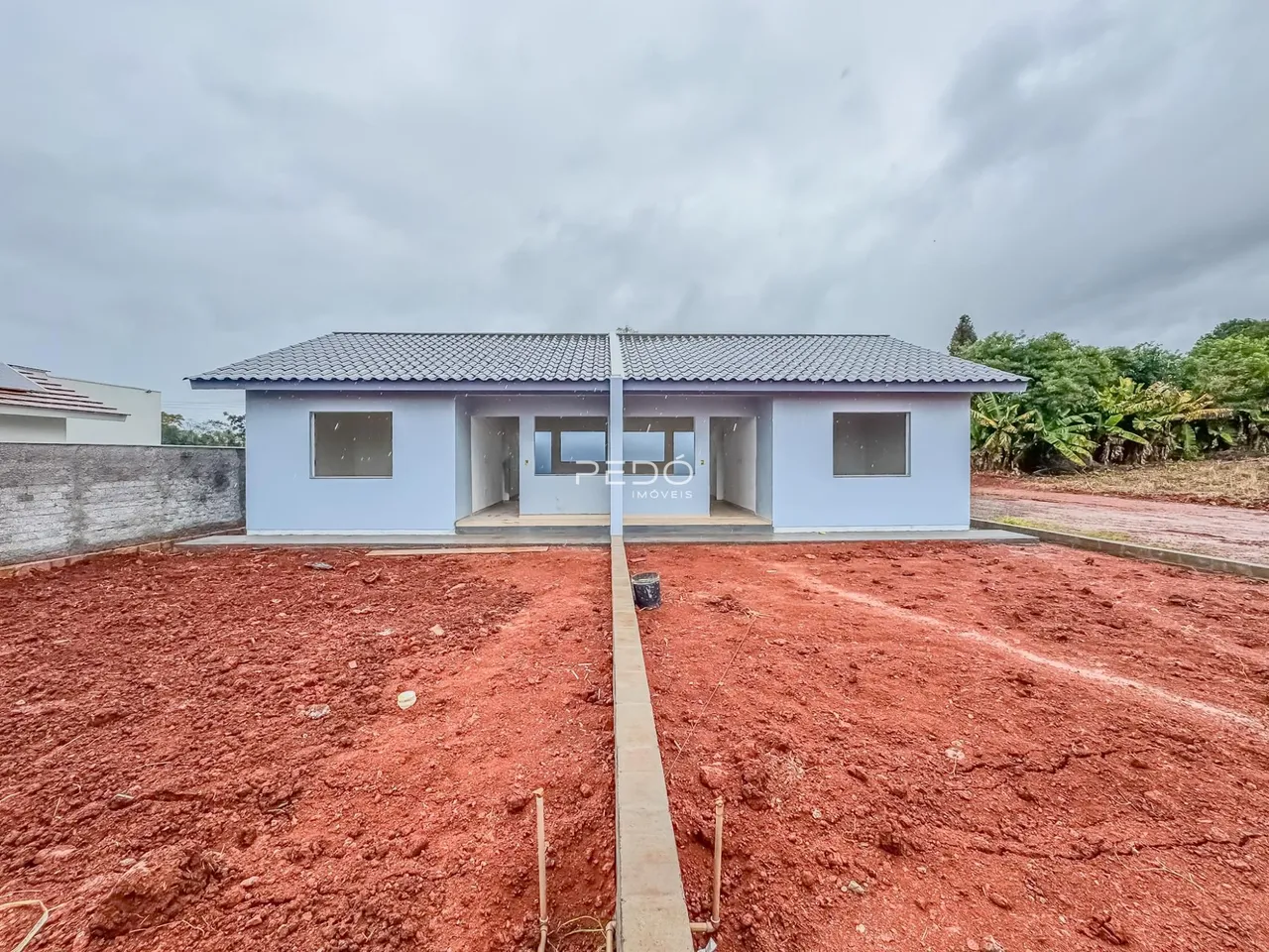 Vista externa de uma casa em terreno com solo avermelhado.