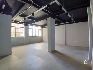 Ambiente interno com estrutura de concreto aparente e grandes janelas.