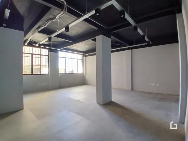 Ambiente interno com estrutura de concreto aparente e grandes janelas.