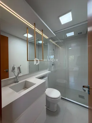 Banheiro moderno com box de vidro e louças brancas.