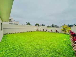 Gramado verde com muro branco e vegetação ao redor da propriedade.
